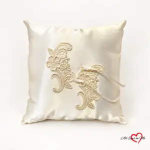 Full view of an off-white satin ring cushion with floral lace and ribbon ties
