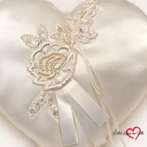 Off-white heart-shaped satin ring cushion with a beaded lace flower, sequinned leaves and ribbon ties.