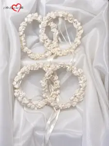 Four handmade white and ivory rose flower crowns with ribbon ties arranged on white fabric
